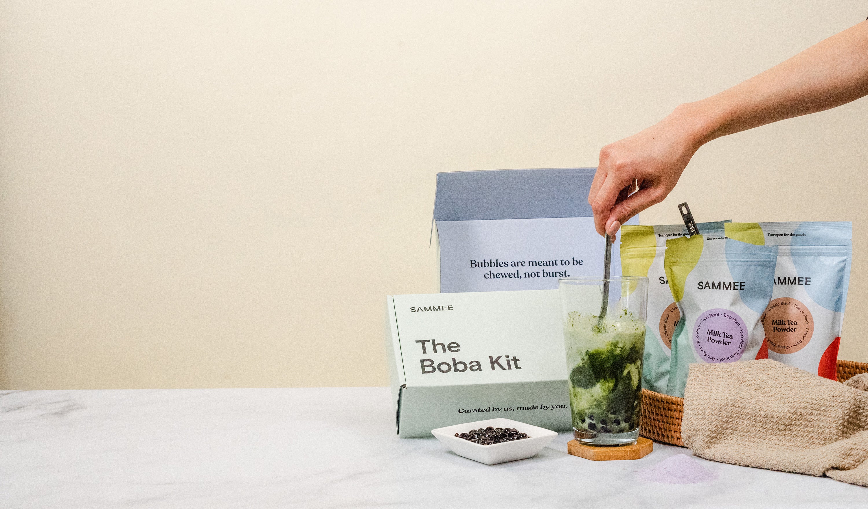 Hand stirring a cup of matcha with SAMMEE packaging in the background